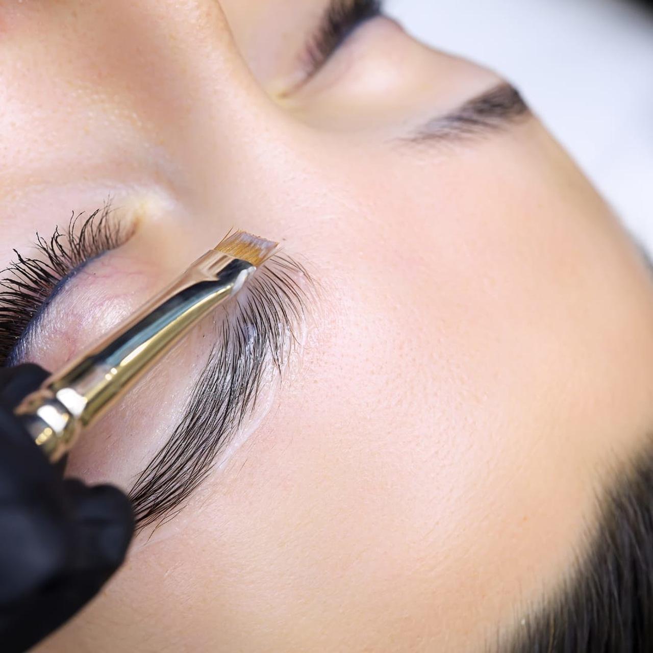 beautician applies paint to client's eyebrows