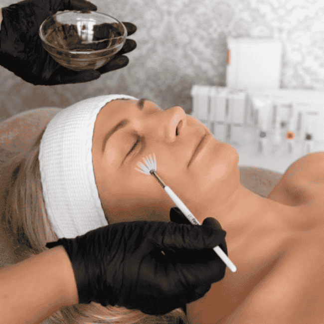 kosmetyczka nakłada na twarz klientki kwasy przy pomocy pędzelka